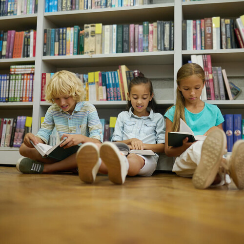 3 Kinder sitzen gemeinsam vor einem Bücherregal auf dem Boden und lesen Header_Kita_und_Schule.jpg